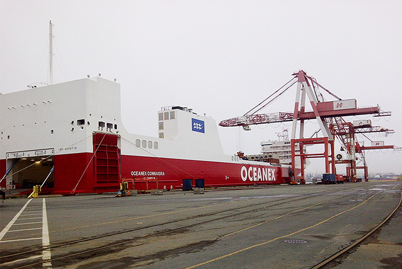 An empty cargo ship at a port with a crane in the background.